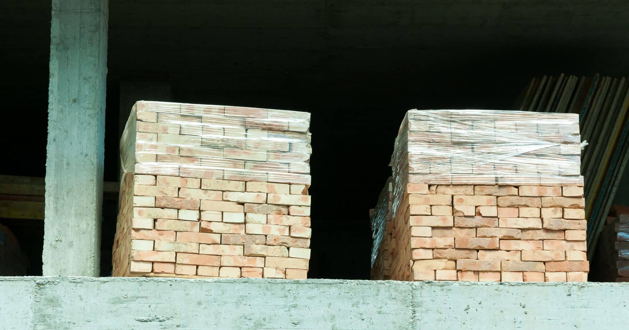 Deux palettes de briques de parement filmées, livrées sur la dalle d'un chantier avant la pose